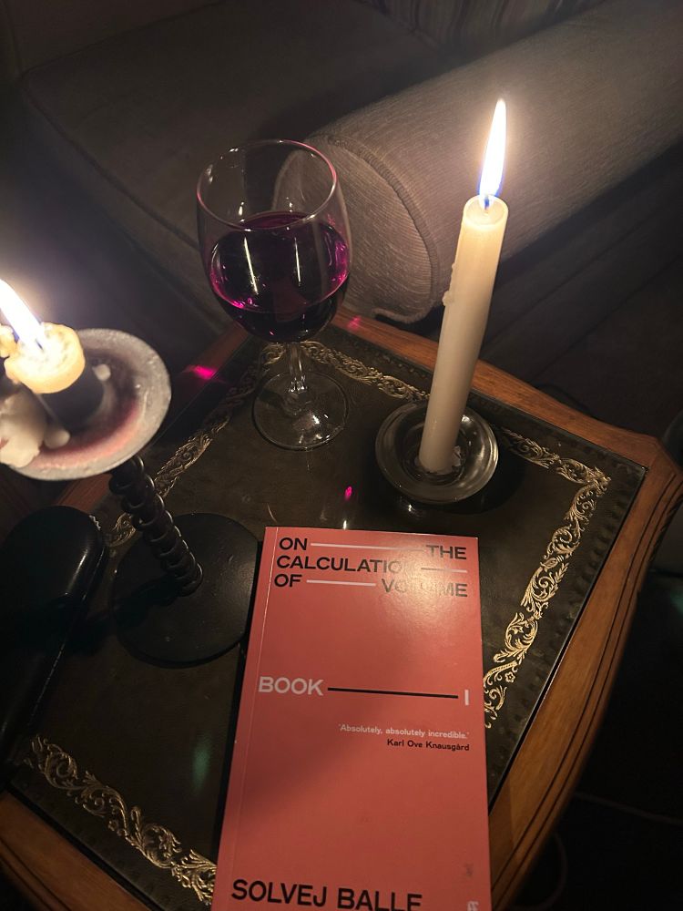 solvej balle’s ‘on the calculation of volume’ sits on a table surrounded by two candles and a glass of red wine