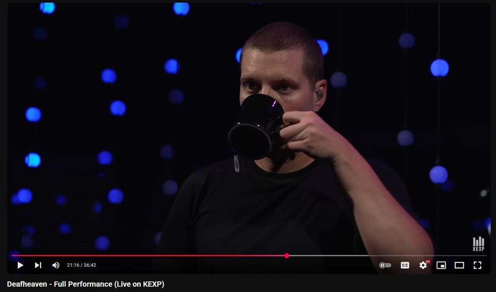 still frame of george clark, singer of deafheaven, sipping from a black mug with a visible tea tag hanging out of it