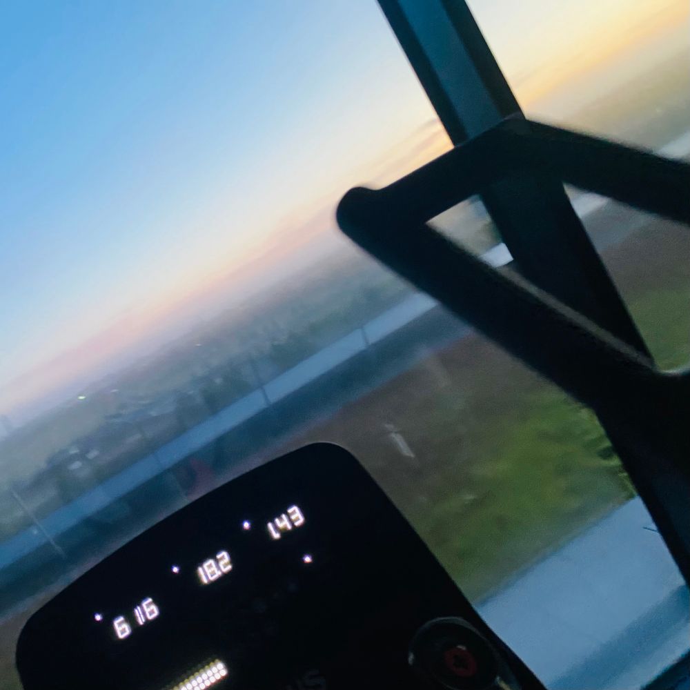 Der vordere Teil eines Crosstrainers vor einer Glasscheibe, durch die der Sonnenaufgang zu sehen ist.