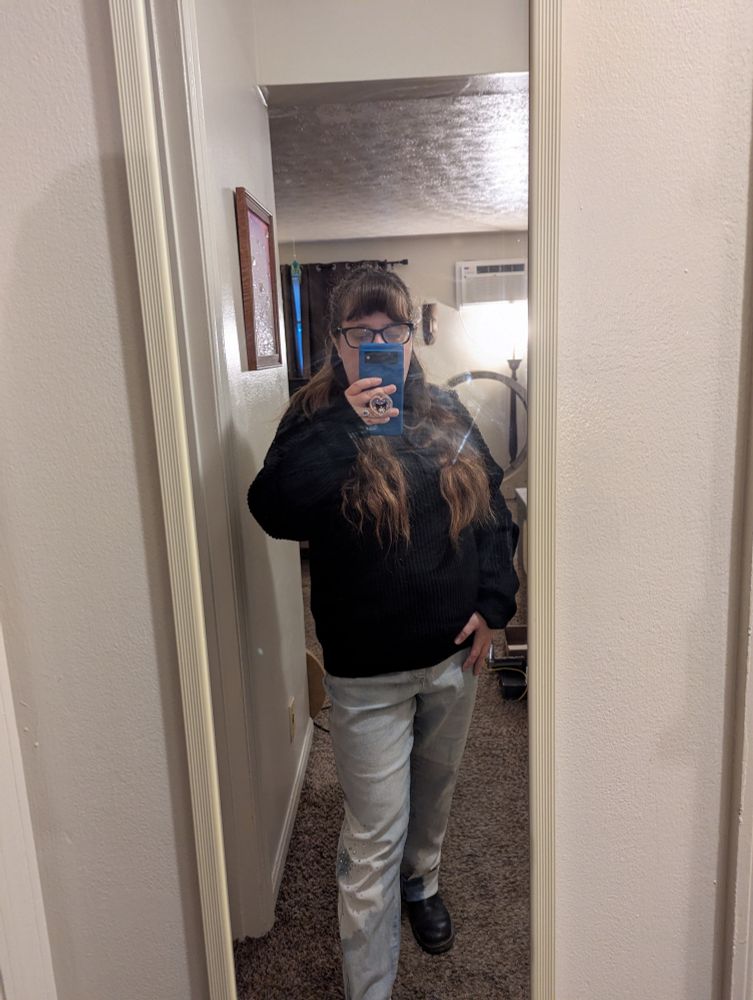 Woman in a half ponytail in black glasses black sweater glittering jeans and black docs