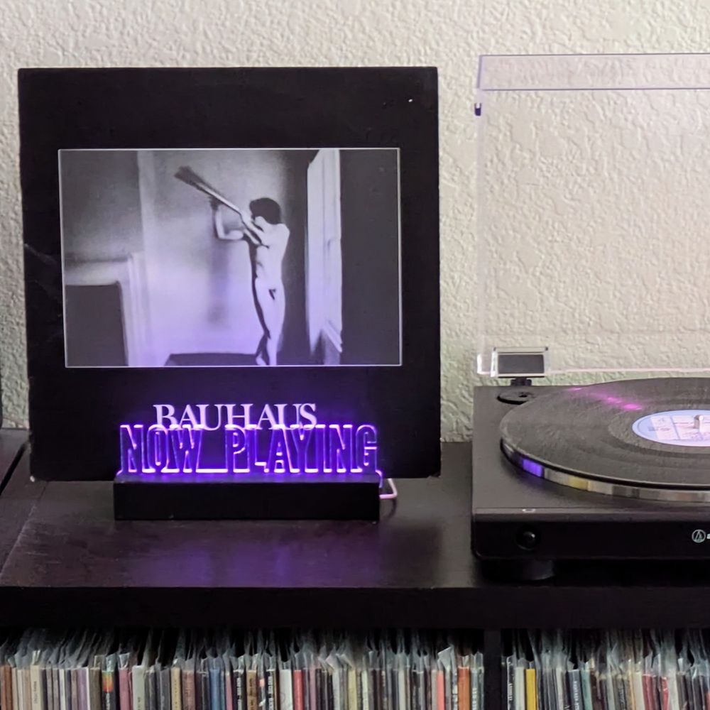 The album cover for "In The Flat Field" by Bauhaus, sitting in a light up Now Playing stand next to a turntable. 