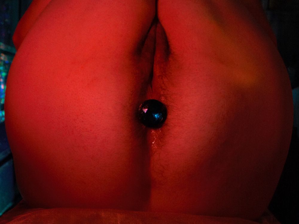 photo of a naked ass and pussy, covered in fuzz and adorned with a blue jeweled butt plug. lit in pinkish orange.