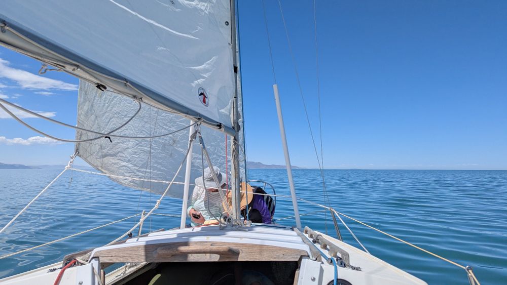 A woman and a young boy sit at the front of a sailboat under sail.