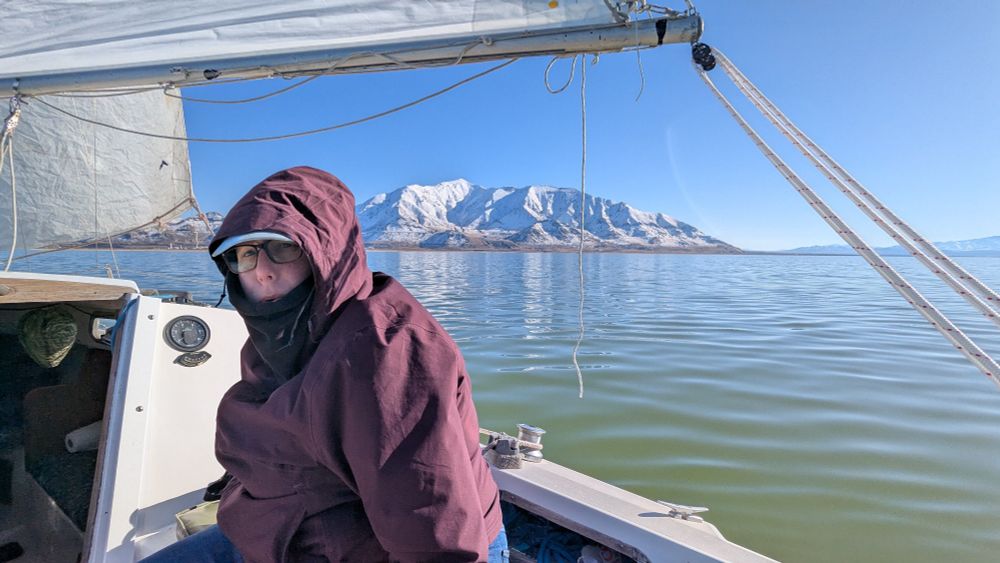 A cold winter sail. A woman in a maroon jacket sits bundled as the boat is moved along by the wind.