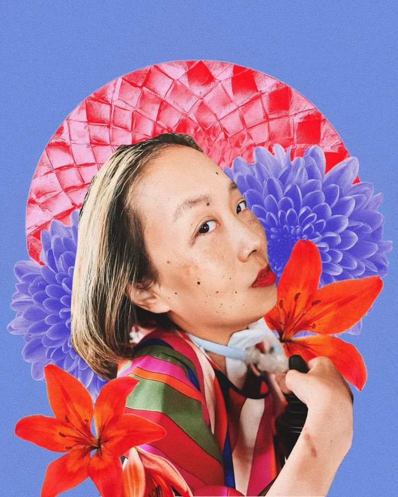 Digital portrait by Jen White-Johnson featuring a photo of Alice Wong, an Asian American woman with honey blonde hair. She is in a wheelchair and there is a tracheostomy at her neck connected to a ventilator. She is wearing a silky multicolored shirt and a bold red lip color. She is looking intently at the camera with the heat of a thousand suns. Behind her are red and purple flowers with a red circle in the background framing her face like a warm sun. The background of the portrait is purple.