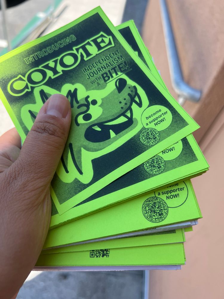 close up photo of hand holding stack of green flyers with cartoon coyote logo
