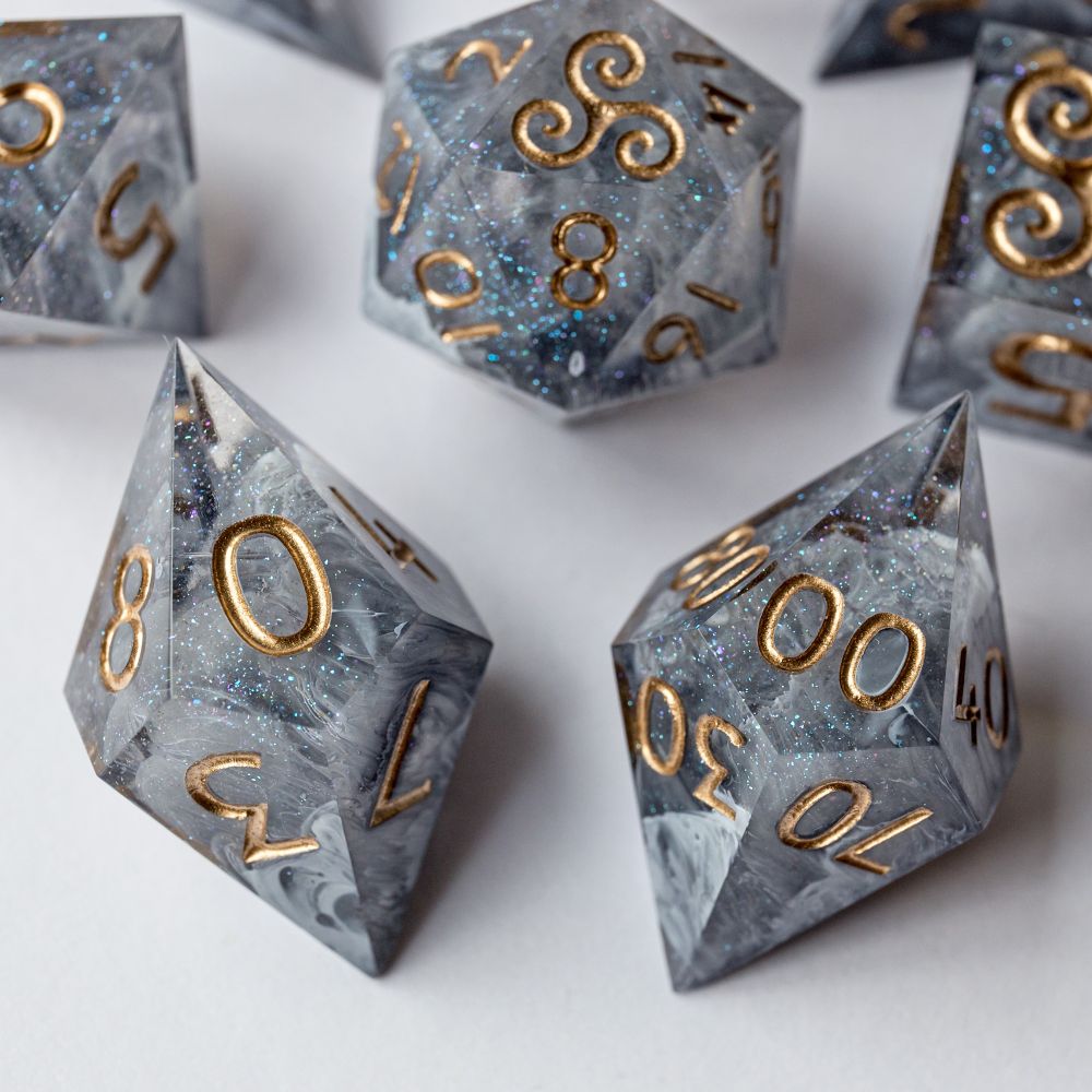 Die Würfel D00 und D10 liegen im Vordergrund scharf im Bild, dahinter sind weitere Würfel des Sets leicht unscharf zu sehen. Alle Würfel haben eine graue Betonstruktur mit goldener Beschriftung.