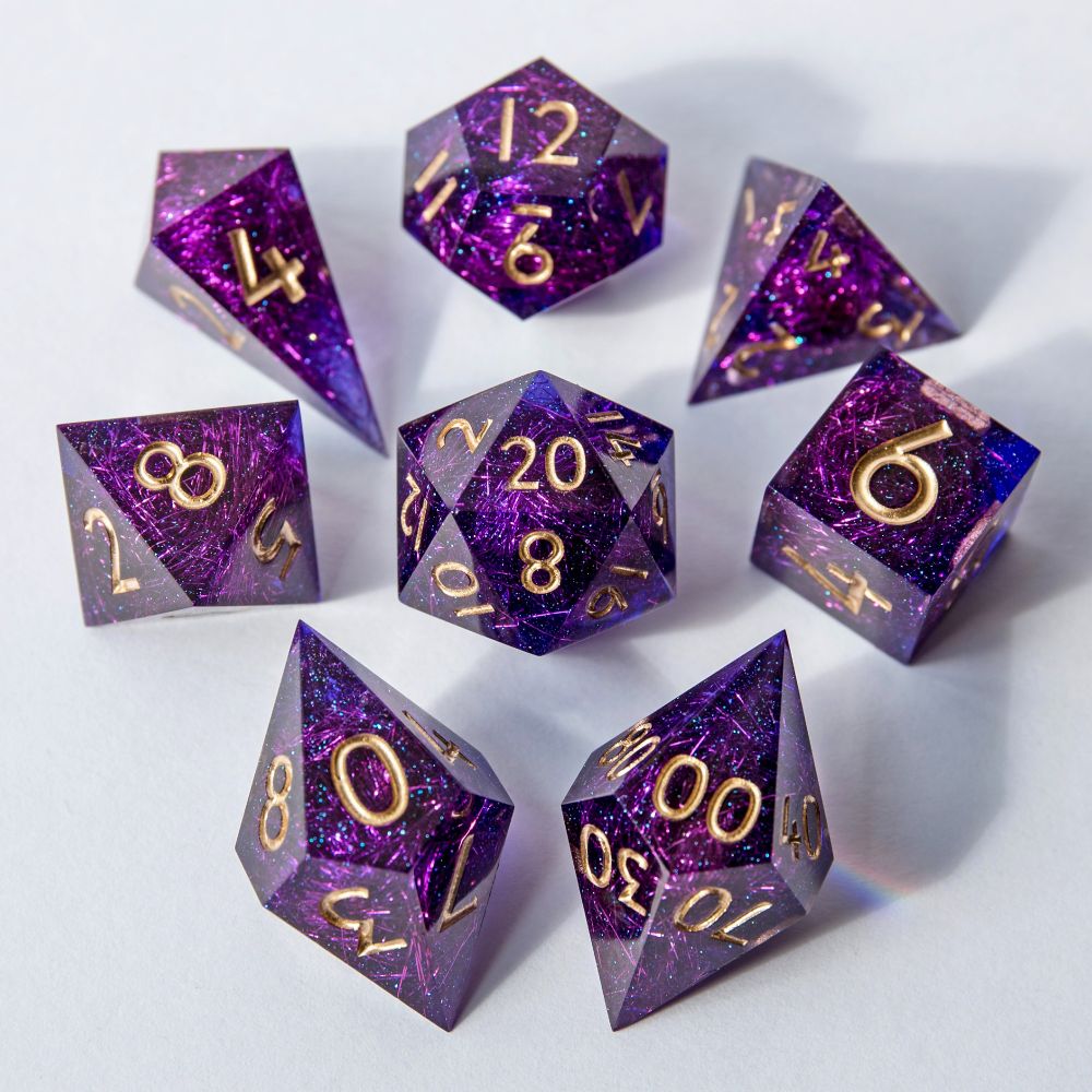 Ein Set aus transparentem violettem Resin, durchzogen von schimmernden Angelina-Fasern und die Nummern sind bemalt mit goldbronzener Farbe. Präsentiert auf weißem Hintergrund. Das Set besteht aus: D4 Shard, D4 Pyramide, D6, D8, D10, D00, D12 und D20.