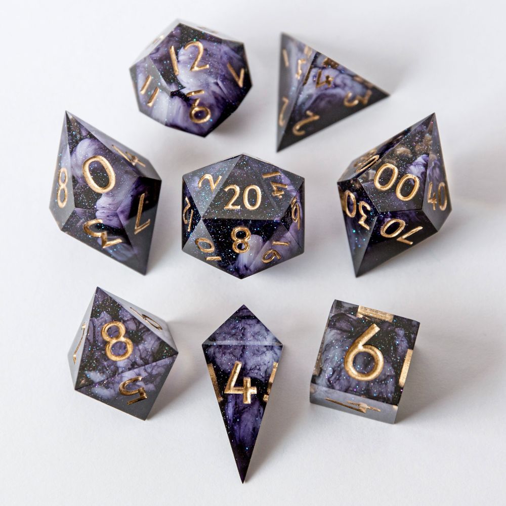 Ein Würfelset aus tief violettem Resin mit goldbronzenen Zahlen und weichen, weißen Swirls im Inneren. Die Würfel liegen auf weißem Hintergrund. Das Set besteht aus: D4 Shard, D4 Pyramide, D6, D8, D10, D00, D12 und D20.