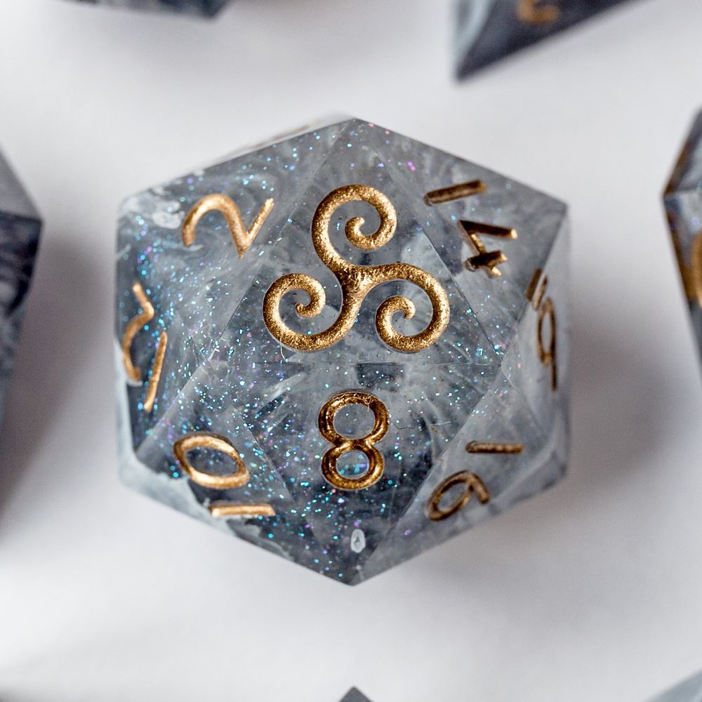 Nahaufnahme eines D20-Würfels auf weißem Hintergrund. Die Zahl 20 ist durch eine Triskele ersetzt. Der Würfel ist grau mit goldener Beschriftung und hat eine Betonoptik.