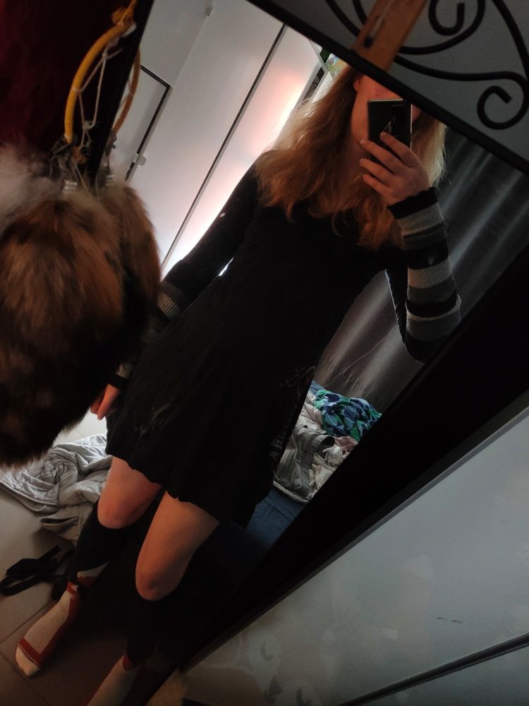 Vrydi wearing a black dress, fox knee socks and arm warmers in front of a full body mirror in her bedroom