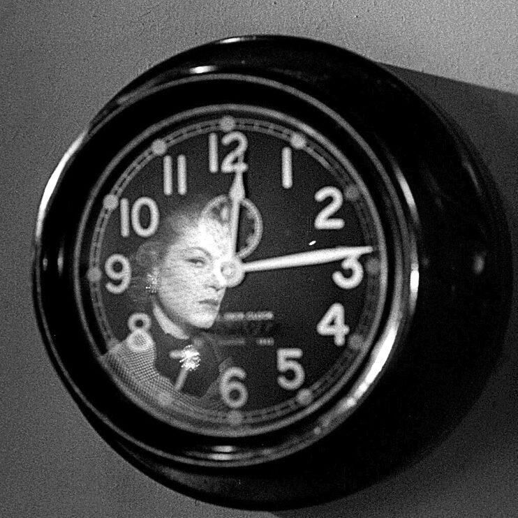 Claire Trevor side eyes her own reflection tensely in a clock on the wall