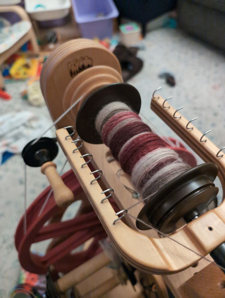 my spinning wheel set up in double drive, with taupe, white, and cranberry red yarn on the bobbin 