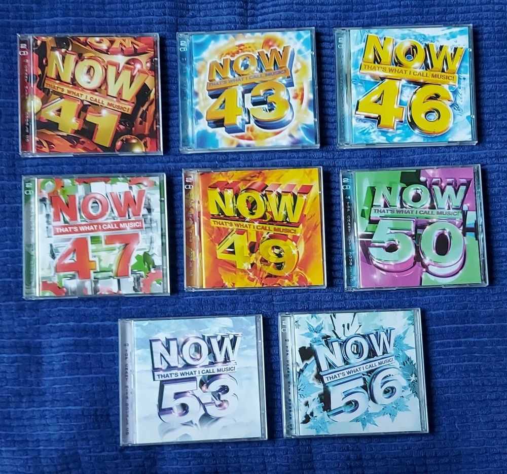 A small collection of "Now that's what I call Music" CDs displayed on a table