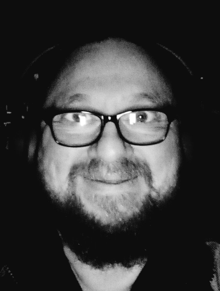 Grinning selfie. Bearded dude with specs and headphones. B&W