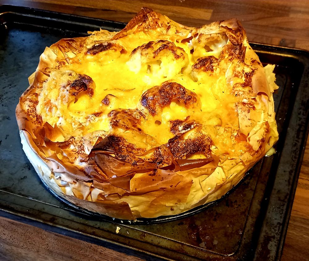Golden-brown cauliflower cheese pie baked in crisp filo pastry, with a bubbling cheese topping and flaky edges, resting on a baking tray.