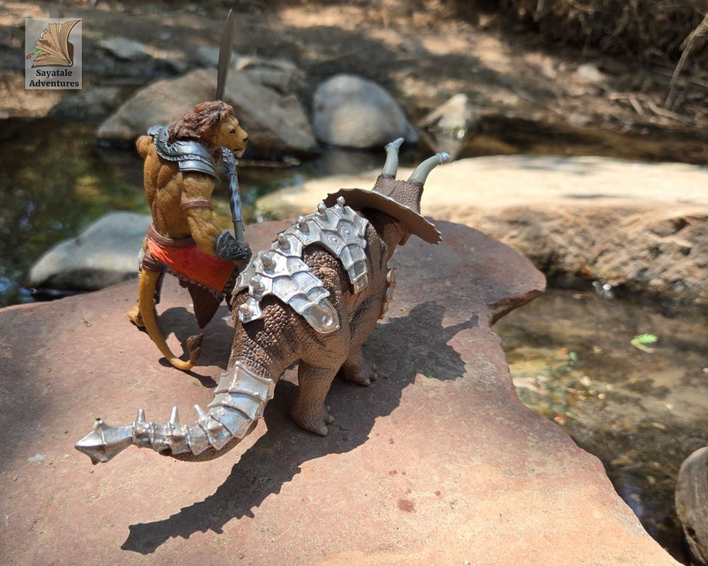 Photo of a toy humanoid lion with an armored triceratops. They are overlooking a stream. 