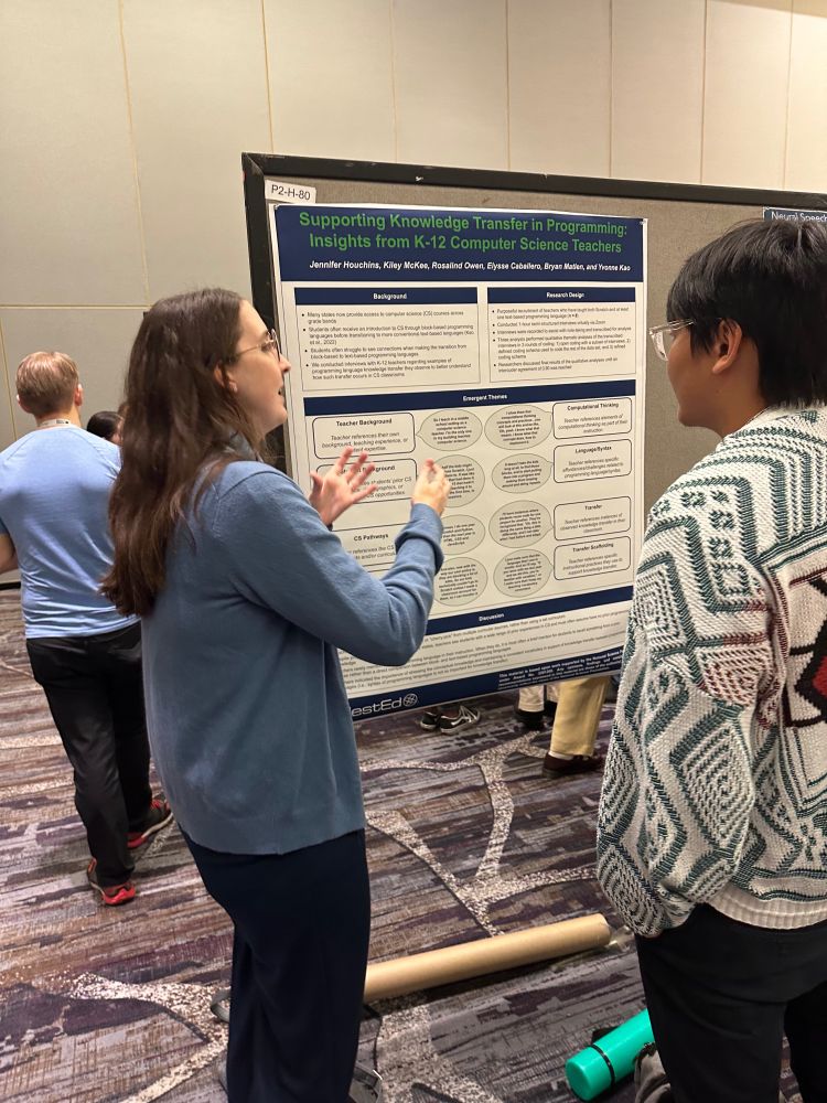 Kiley gesturing to academic poster on CS teacher interviews while discussing research with conference participant. 