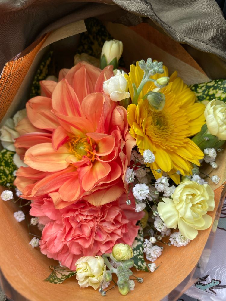 花束。全体にやさしいオレンジ系。オレンジのダリアとカーネーション、黄色のガーベラとクリーム色のスプレーカーネーション、ストック、かすみそう。黄色い斑入りの葉。