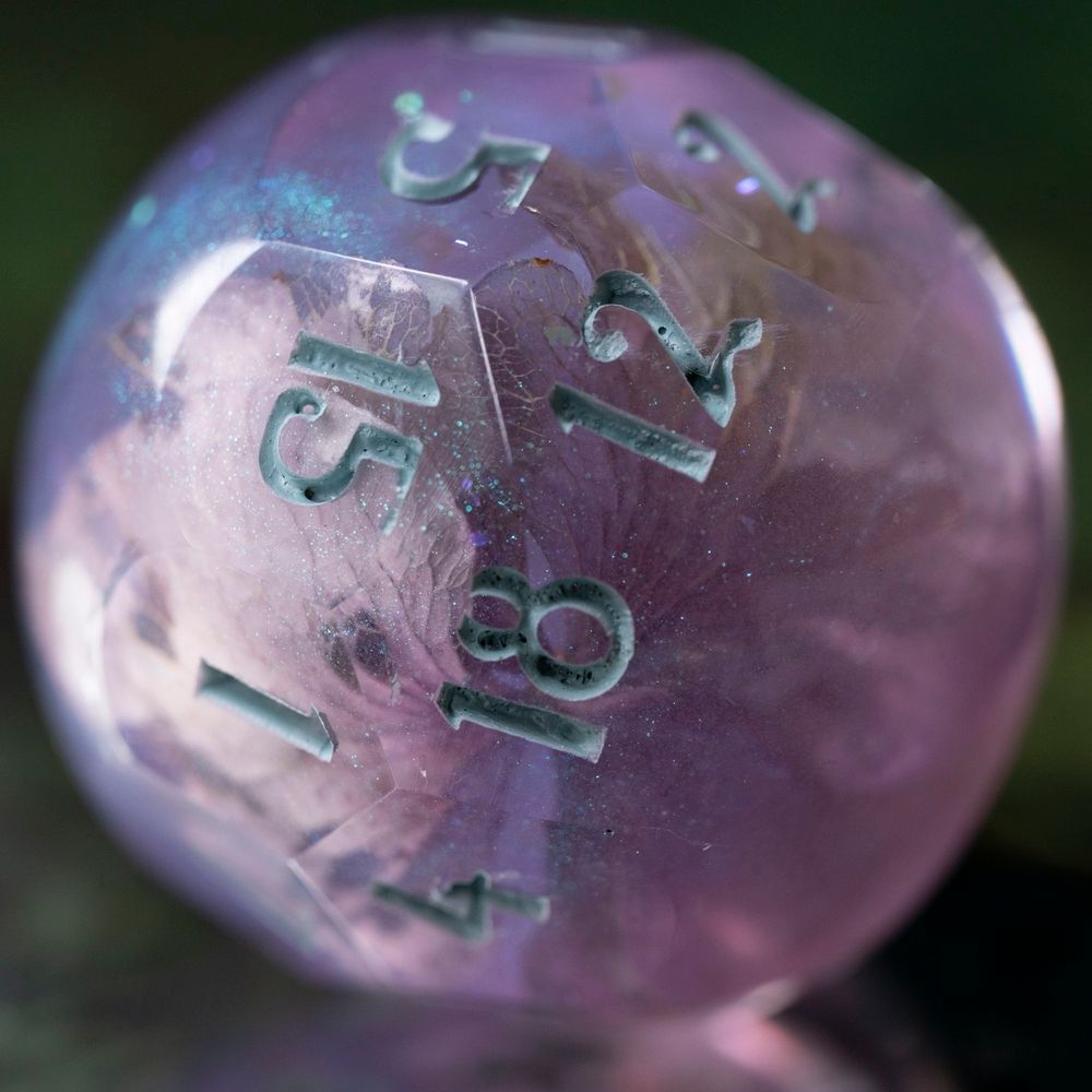 A 20-sided die in the shape of an orb, made of blue-purple iridescent resin with a hydrangea flower inclusion