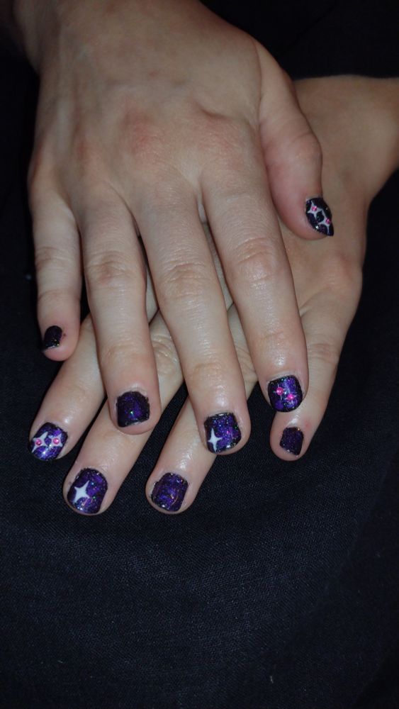 Picture of hands with nails painted with a dark, glittering purple swirl. Pink and white stars adorn several fingers.