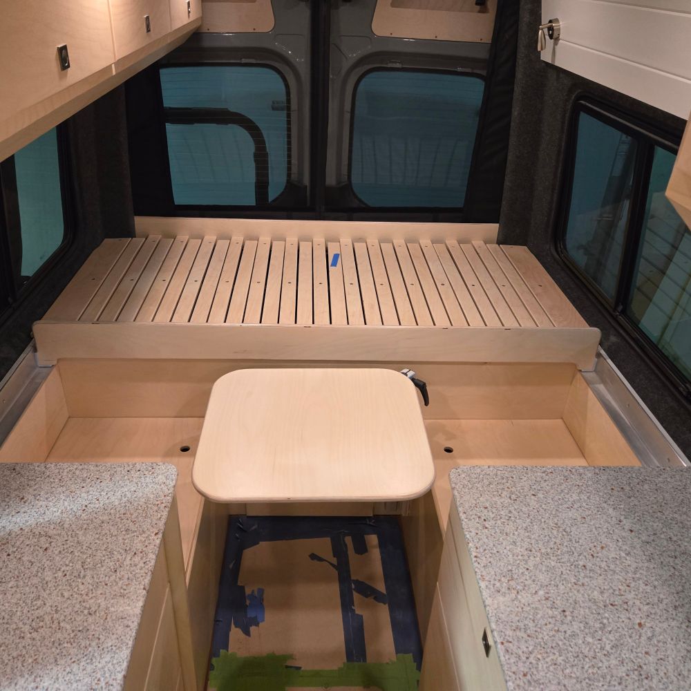 This downwards view shows off the colors of the countertops and the small stow-away table made from the same baltic birch plywood as the counters and benches. Behind the table is a bed frame that slides forwards into a full sizes frame.