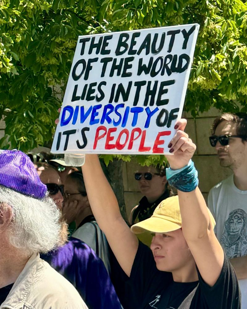 A person holds a sign that says, 'The Beauty of the World lies in the Diversity of it's People'