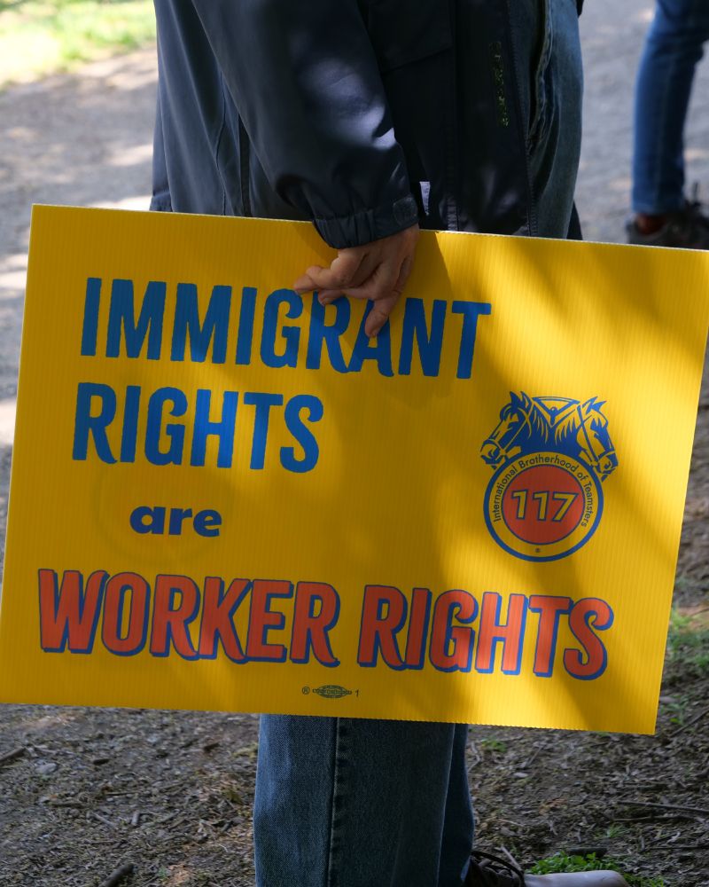 A worker with Teamsters local 117 holds a sign at their side that says, 'Immigrant Rights are Worker Rights'
