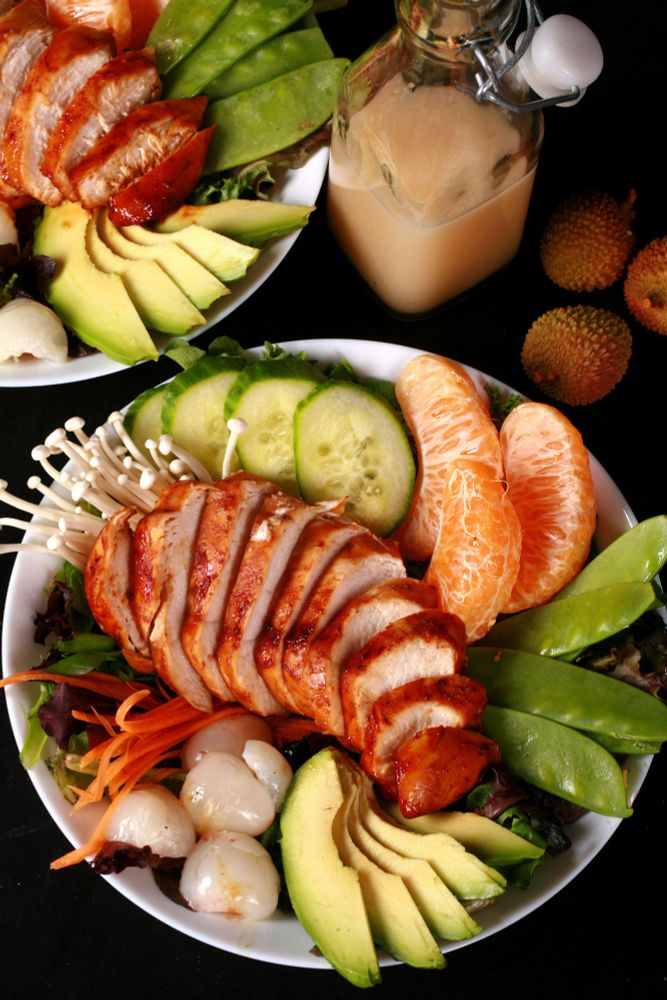 2 Asian inspired salads with lychee balsamic glazed chicken on top, and a bottle of lychee dressing. 