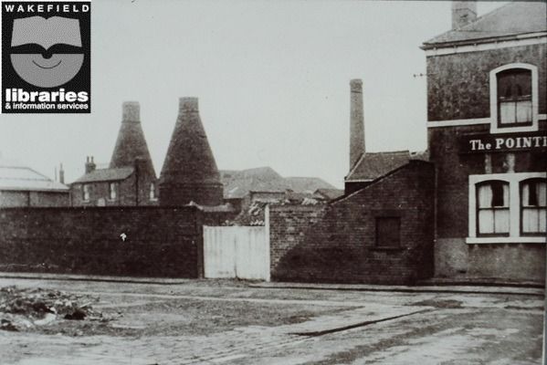 A black and white photograph of a brick wall in front of conical chimneys.