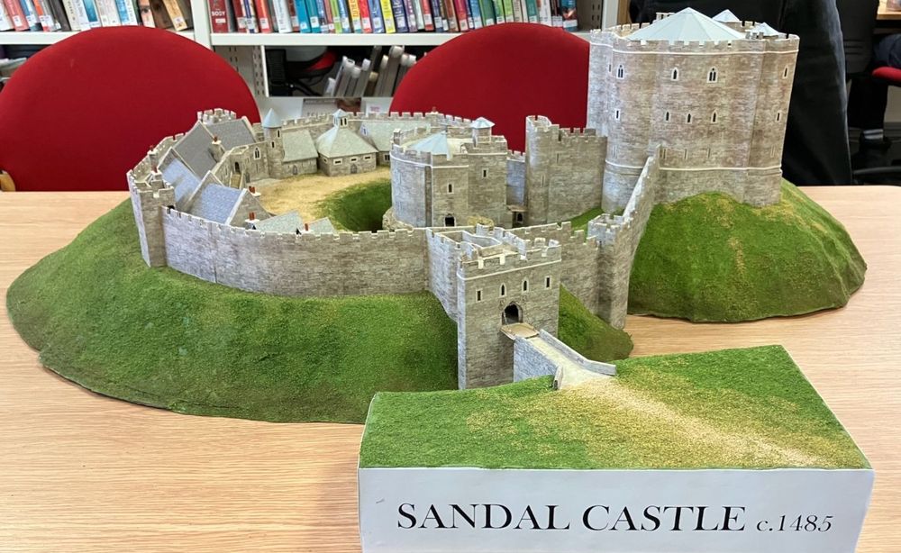 A model of Sandal Castle on a table in front of bookshelves.