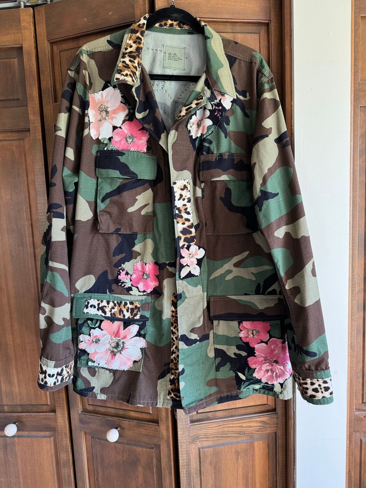 Green, brown, tan and black military jacket front has been embellished with coral/pink tropical flowers on the lower pockets and upper chest. Bits of leopard print fabric have been strategically placed on the cuffs, on one lower pocket flap, and on the button placket. 