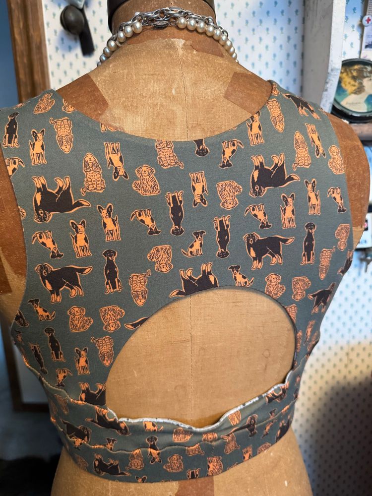 Antique mannequin modeling a sportsbra made from olive green athletic material with orange and black dogs (back view). 