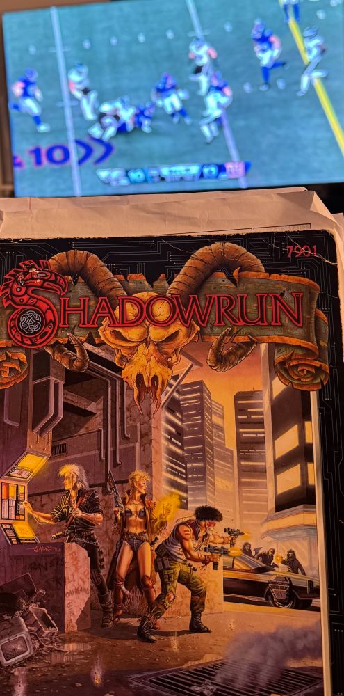 Eagles vs Giants game in the background on the tv and Shadowrun Second edition Corebook in front of it. 
