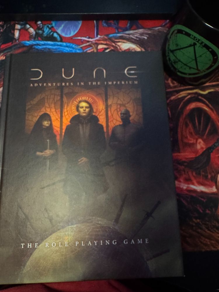 Cover of Dune Adventures in the Imperium on a Haunted West mousepad next to a Delta Green coffee cup.