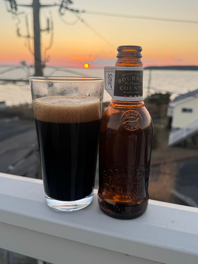 Goose Island bourbon county in a chilled glass with sunset behind it. 