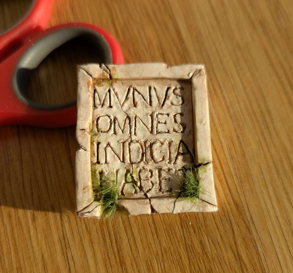 Photograph of a tiny polymer clay 'plaque' made to look like old marble, cracked and moss covered. Engraved are the words "MVNVS OMNES INDICIA HABET".
#taskmaster #latin #latinlanguage #alexhorne #fanart #polymerclay #mixedmedia