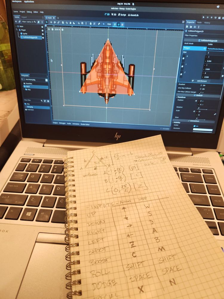 Photo: an open laptop with Godot project editor open. A spaceship with a red triangle marked over it on screen. Notebook on keyboard with math and button assignments written on graph paper