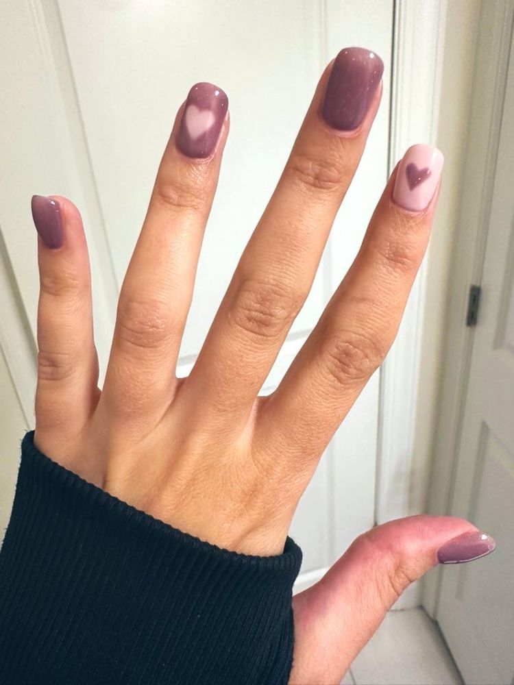 photo of hand showing off structured gel manicure in purple with pink heart and accent nail that’s pink with a purple heart