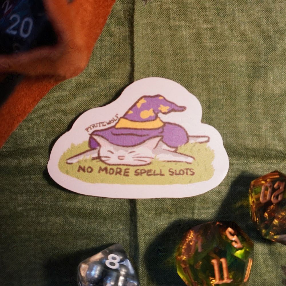 sticker of a wizard kitty laying in the grass under his giant purple wizard hat. written in the grass is "no more spell slots".