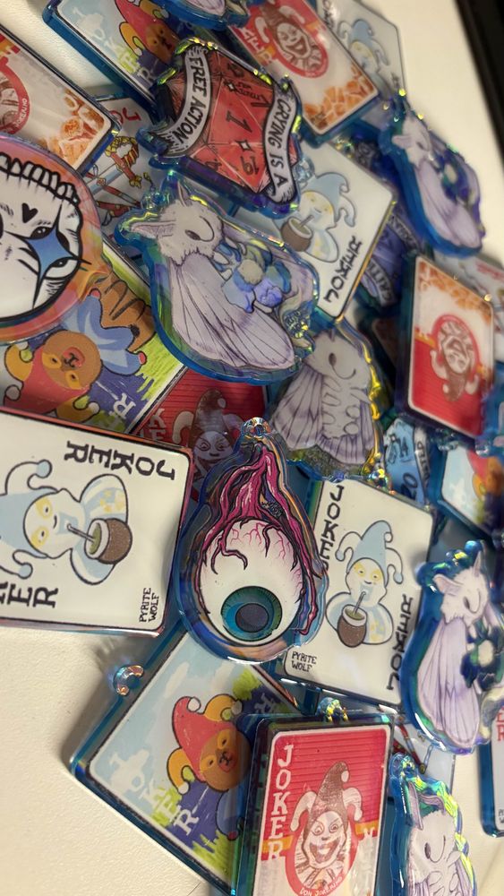 a pile of acrylic keychains based on my designs: moths, original balatro jokers, skulls, eyes