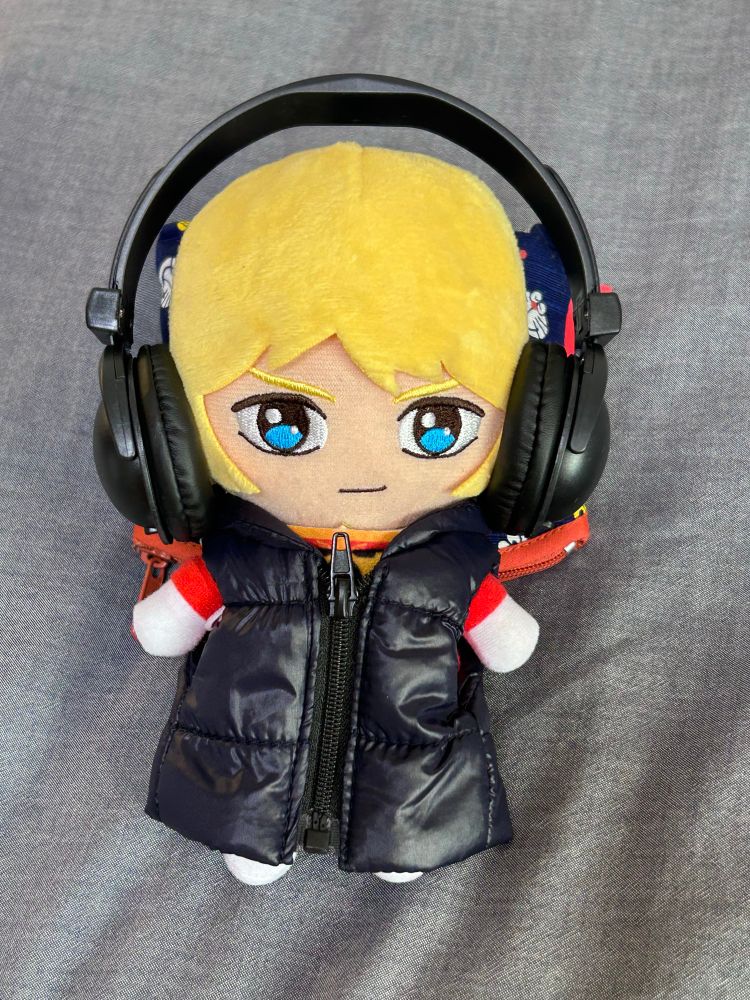 ヘルメットを外した状態でヘッドホンとダウンベストを着ているシャアのぬいぐるみ ベストの前のファスナーを閉めている