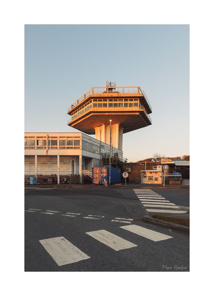 a large concrete tower shaped like an air traffic control tower. There are zebra crossings leading to it (and to other, less exciting buildings) and the sun is golden on one side of it.