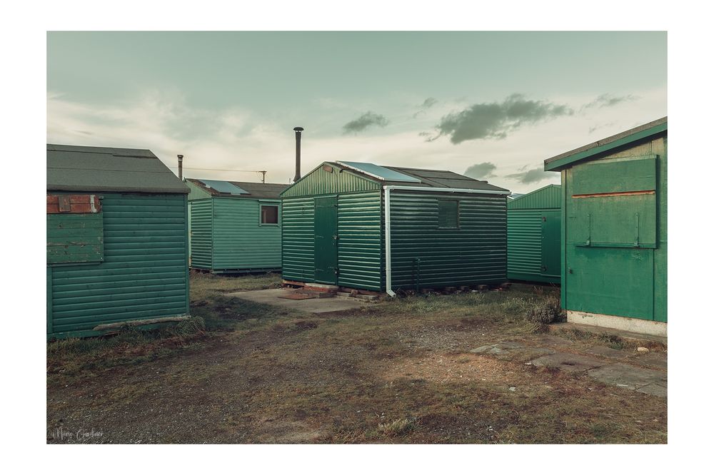 green wooden fishing huts with metal chimneys, standing in rows