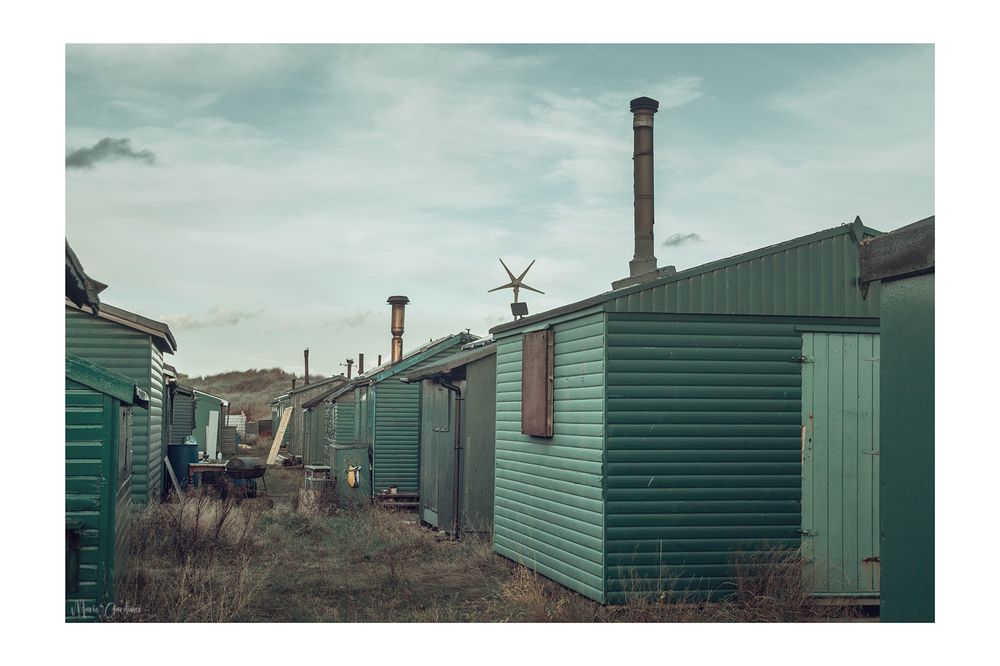green wooden fishing huts with metal chimneys, standing in rows, looking at them side on
