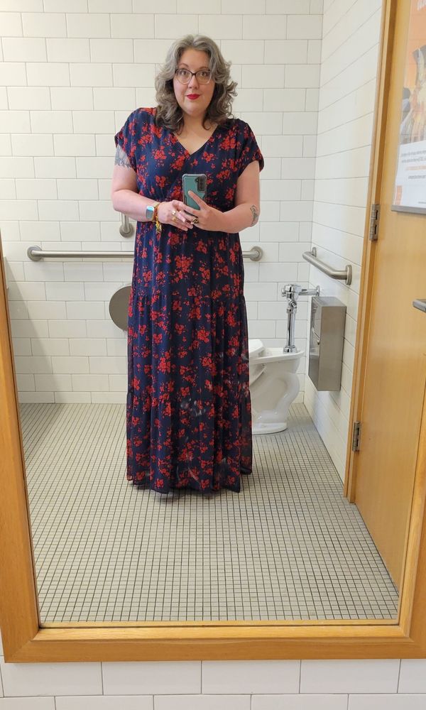 An anxious gray-haired woman wearing too much eye makeup and a cute blue dress with red flowers 