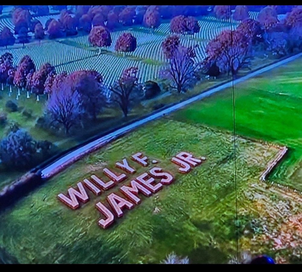 In a large green meadow the name Willy F. James Jr. is spelled
The picture is taken from above and you can see the military cemetery with its white crosses adjacent 