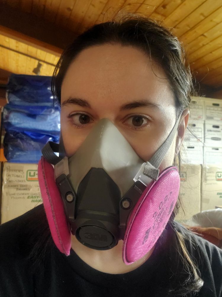 Me, a white person with dark brown hair in a black shirt. On my face is a heavy duty half face 3m mask with pink filters on each side