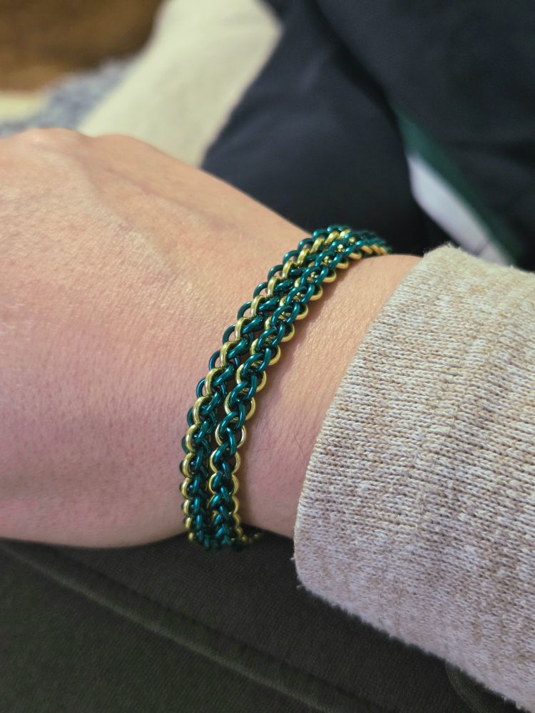 A chainmaille bracelet, two lengths of JPL3 in teal in a line of yellow. Worn on my wrist. 