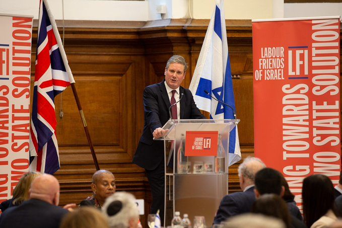 Starmer in front of UK and Israeli flags giving speech to Labour Friends of Israel.